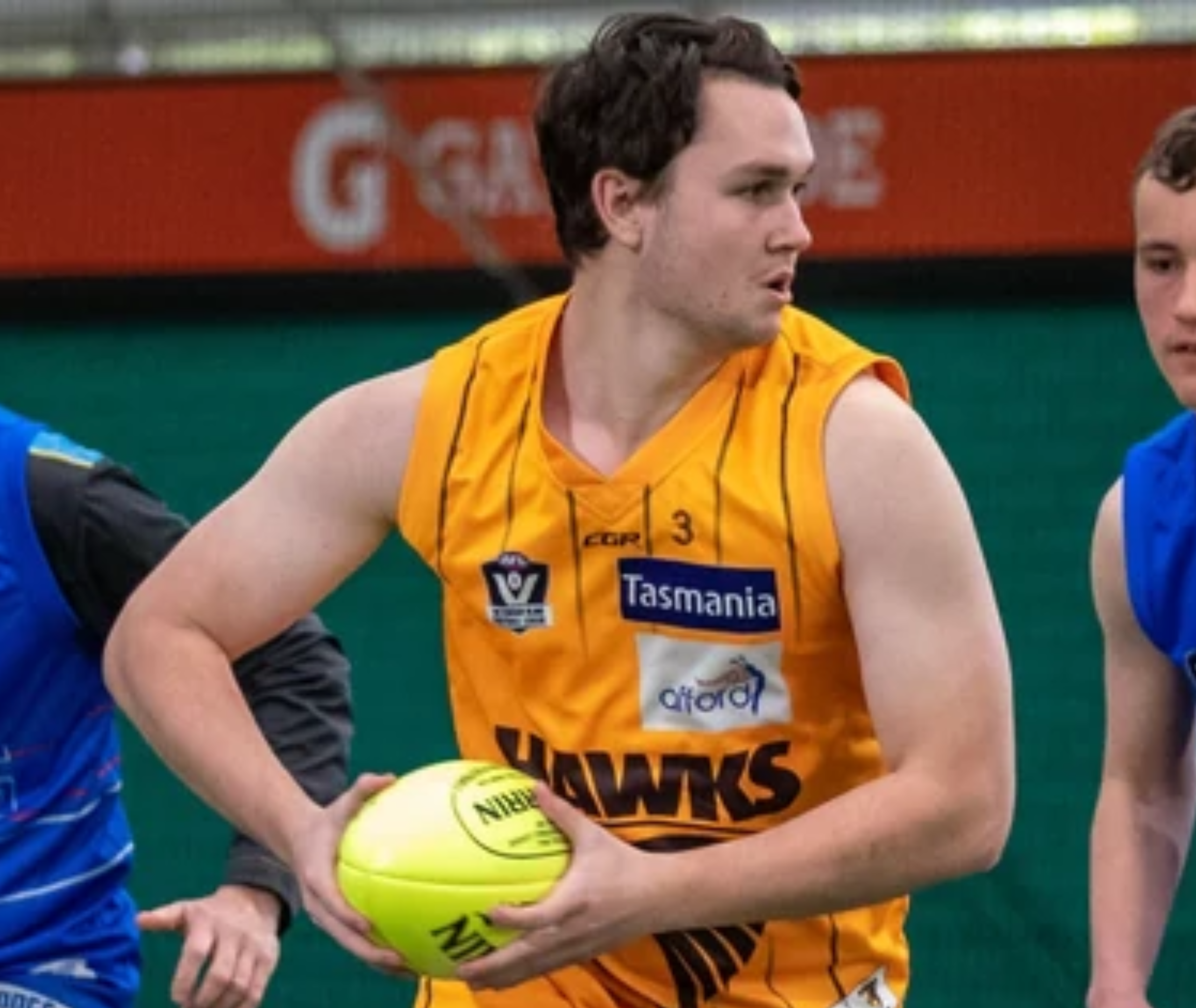 Close up image o0f Jhonny. He is playing footy and running. He has a footy in his arm and he is wearing the Hawthorn top.