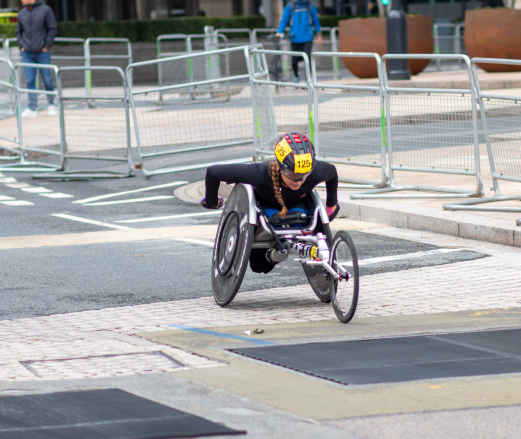 Female para-athlete racing down a street in a racing wheelchair.