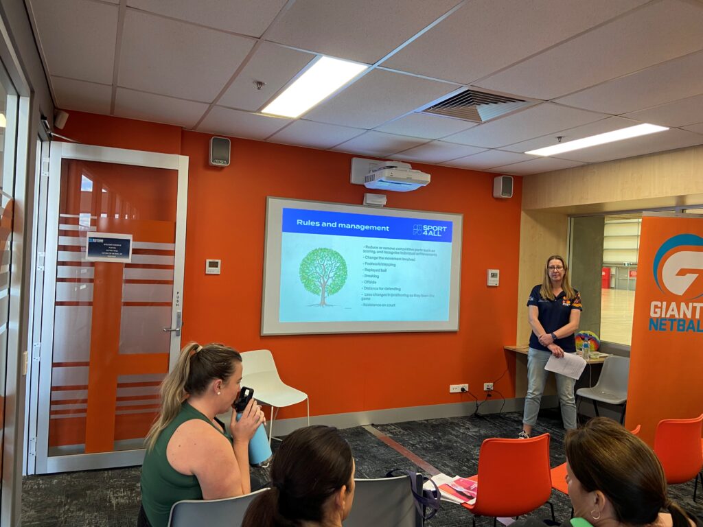 Sport4All Inclusion Coach Jenny presenting to an audience seated in chairs, attentively listening.