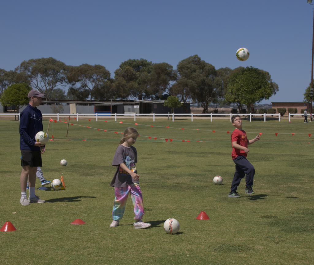 Kids playing soccer on a soccer field. The coach is observing the session.