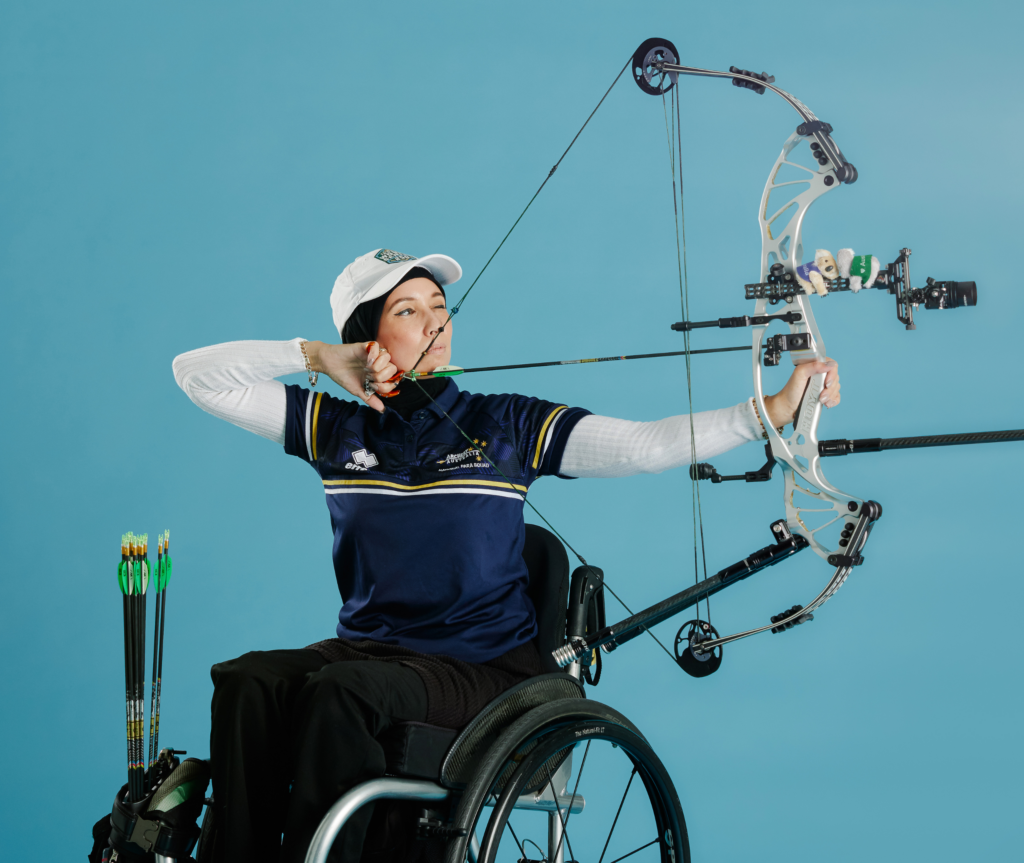 A wheelchair archer is aiming her bow on a green background.