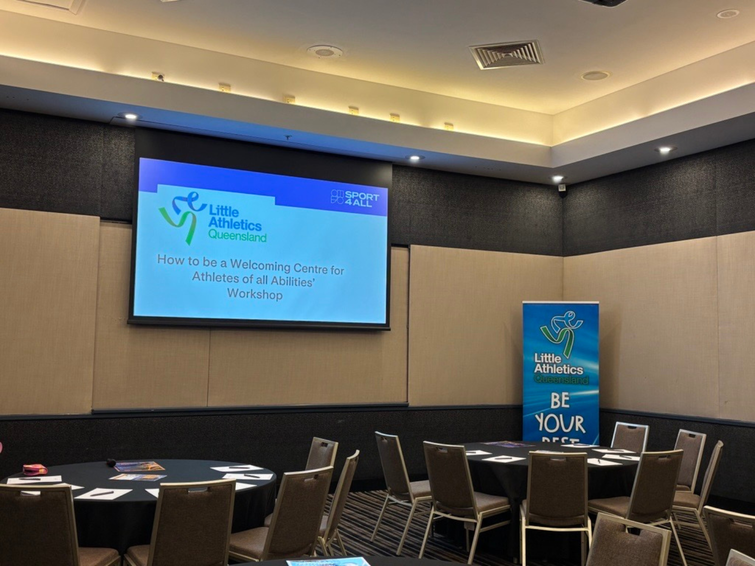 A projector screen shows the title slide for a workshop co-hosted by Little Athletics Queensland and Sport4All.