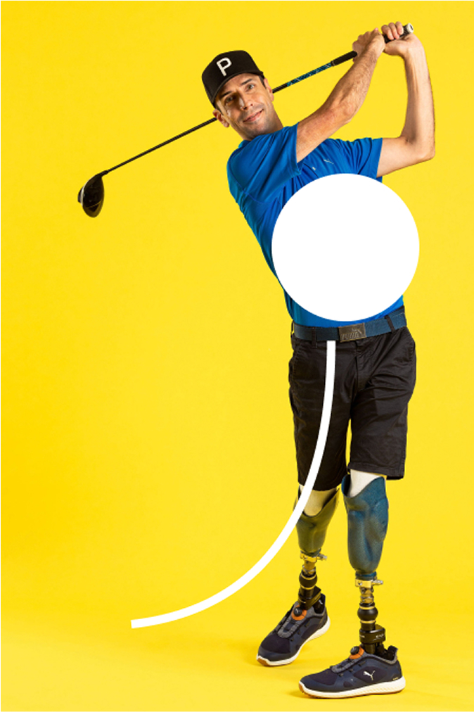 A golfer with prosthetic legs, wearing a blue shirt, is captured mid-swing in a studio against a yellow background.