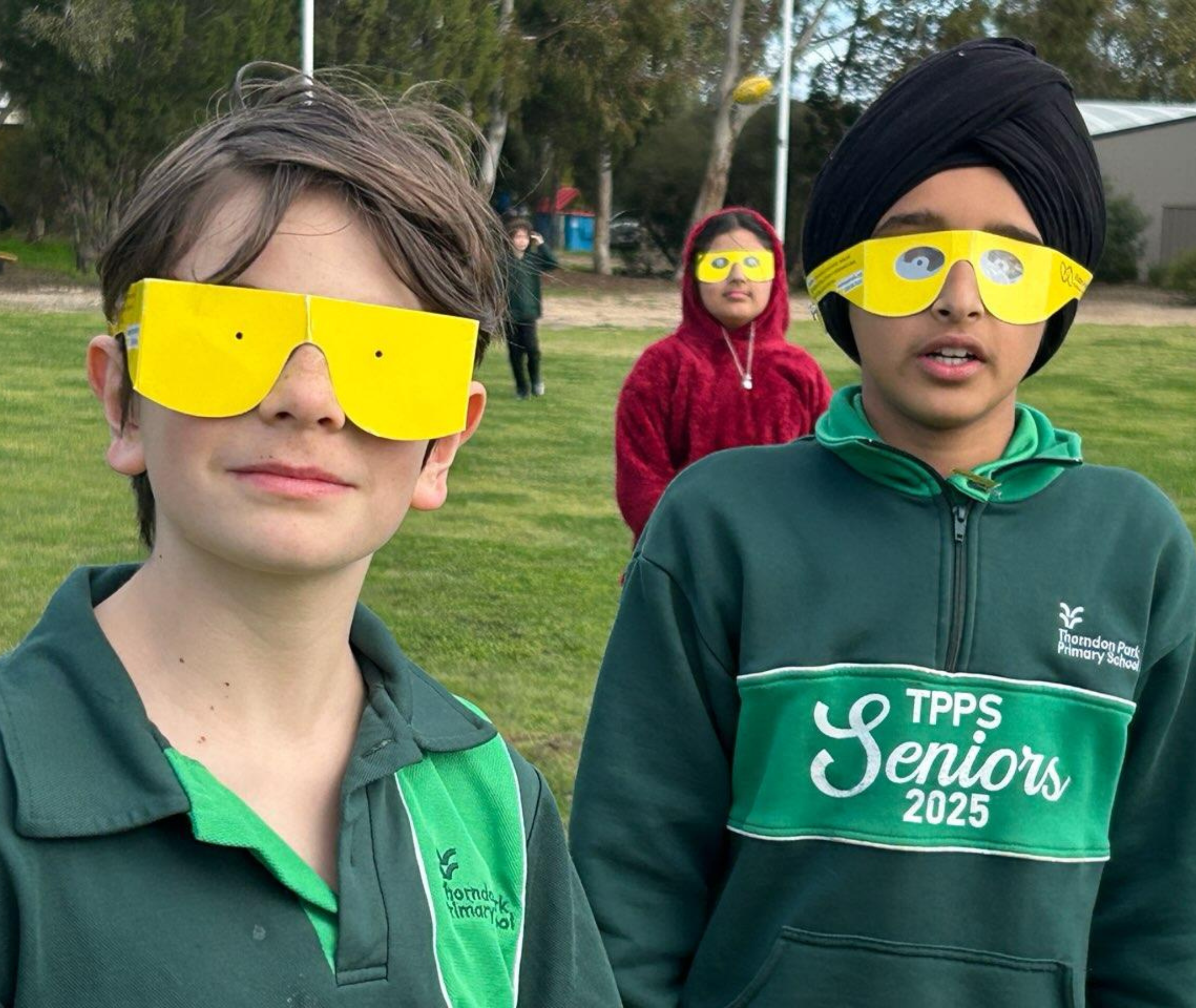 Close-up of two students wearing yellow simulation glasses, one in a green sports jacket and the other in a green hoodie with “TPPS Seniors 2025” on the front.