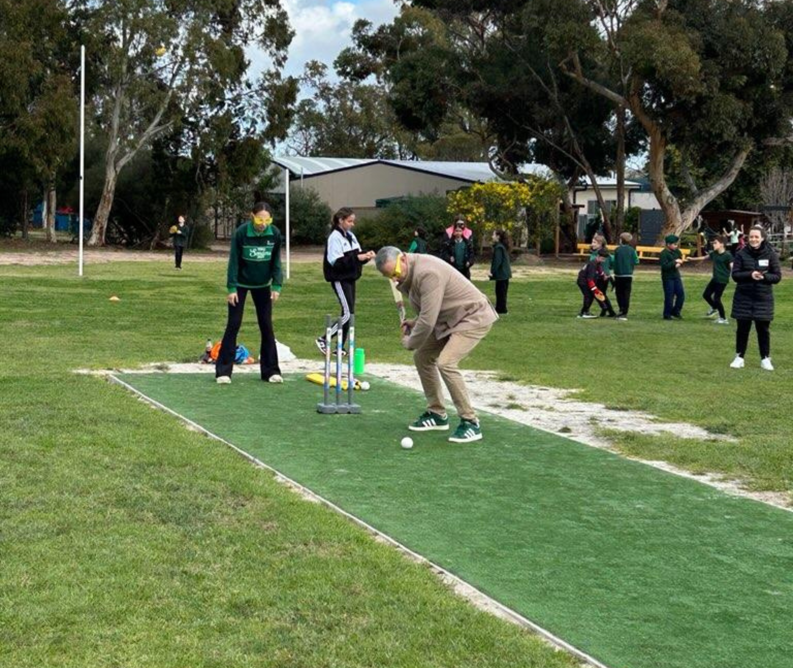 Adult and student playing cricket on an outdoor pitch, both wearing yellow simulation glasses