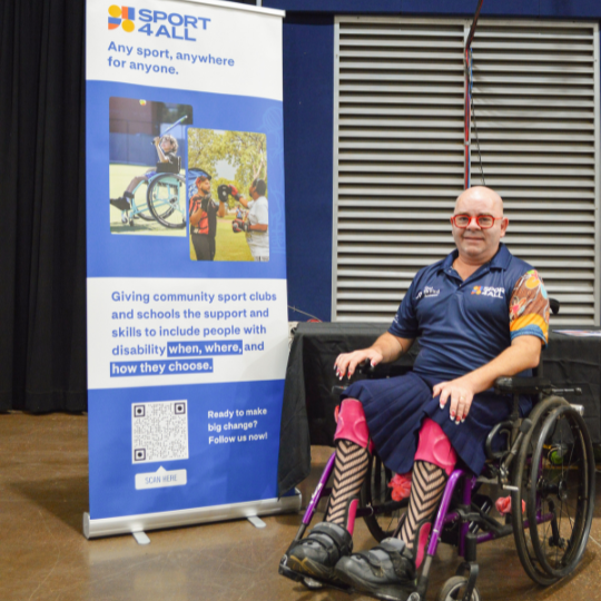 David Hydon, Sport4All Inclusion Coach sits in a wheelchair beside a Sport4All banner at a community event.