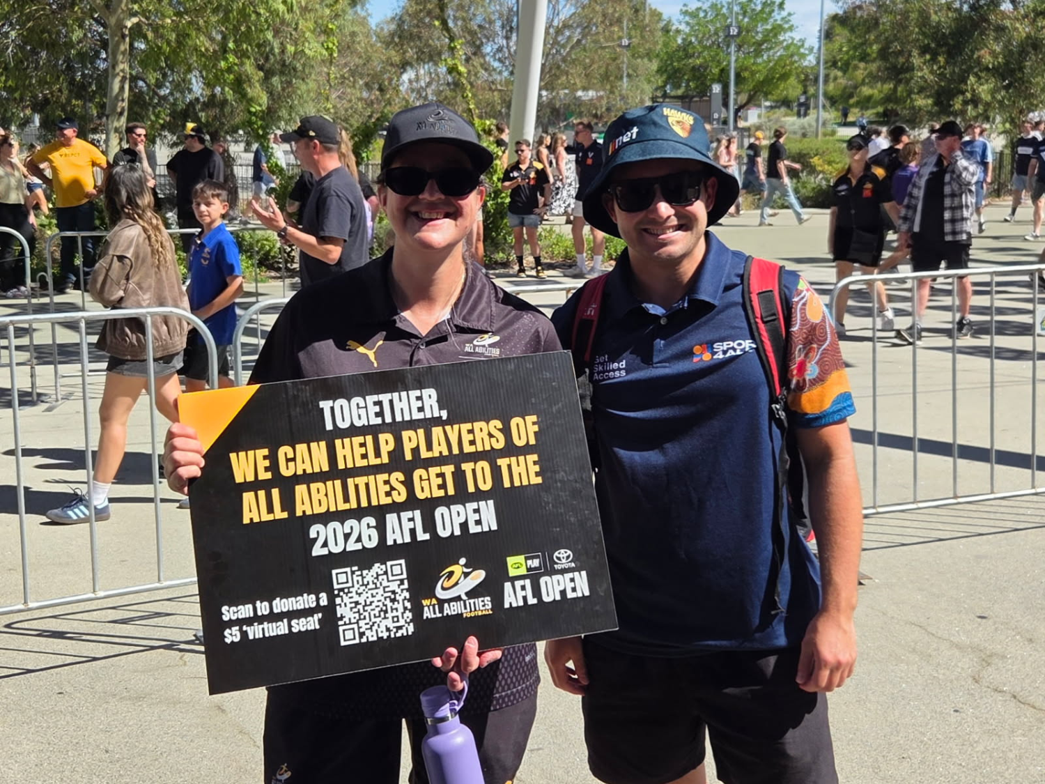 Two people smile while holding a sign promoting access to the 2026 AFL Open.