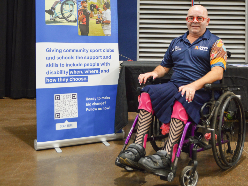 David Hydon, Sport4All Inclusion Coach sits in a wheelchair beside a Sport4All banner at a community event.