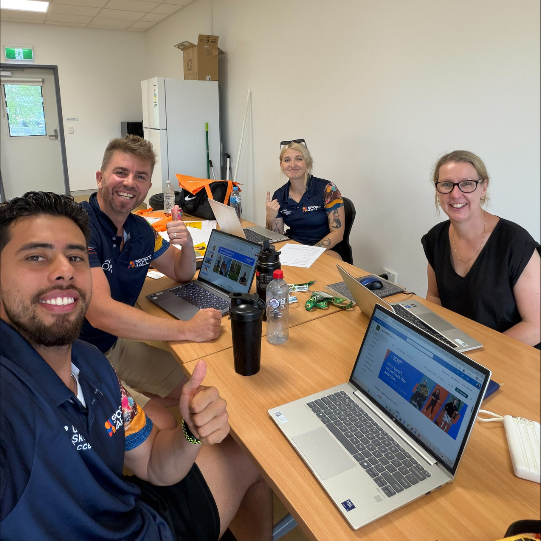 Sport4All team members sit around a table working on laptops in a meeting room.