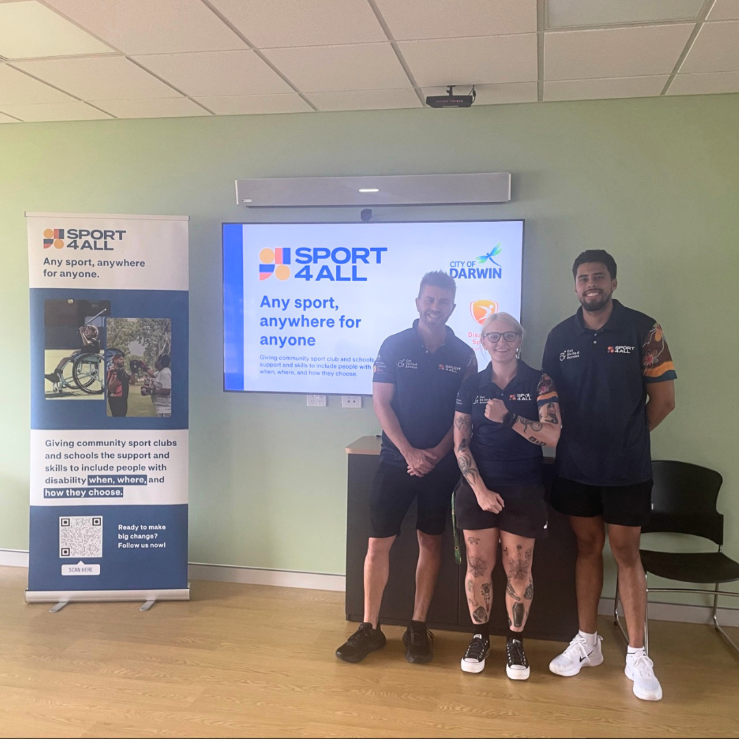Three Sport4All team members stand in front of a presentation screen and banner.