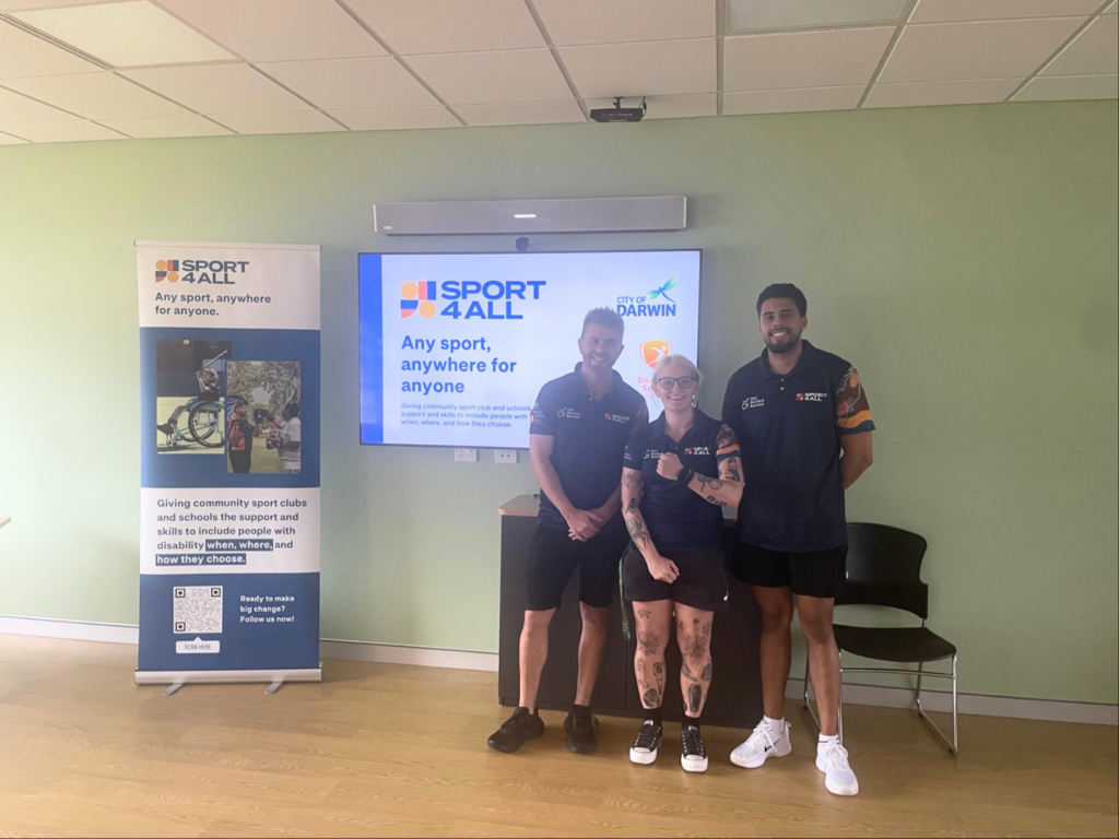 Three Sport4All team members stand in front of a presentation screen and banner.