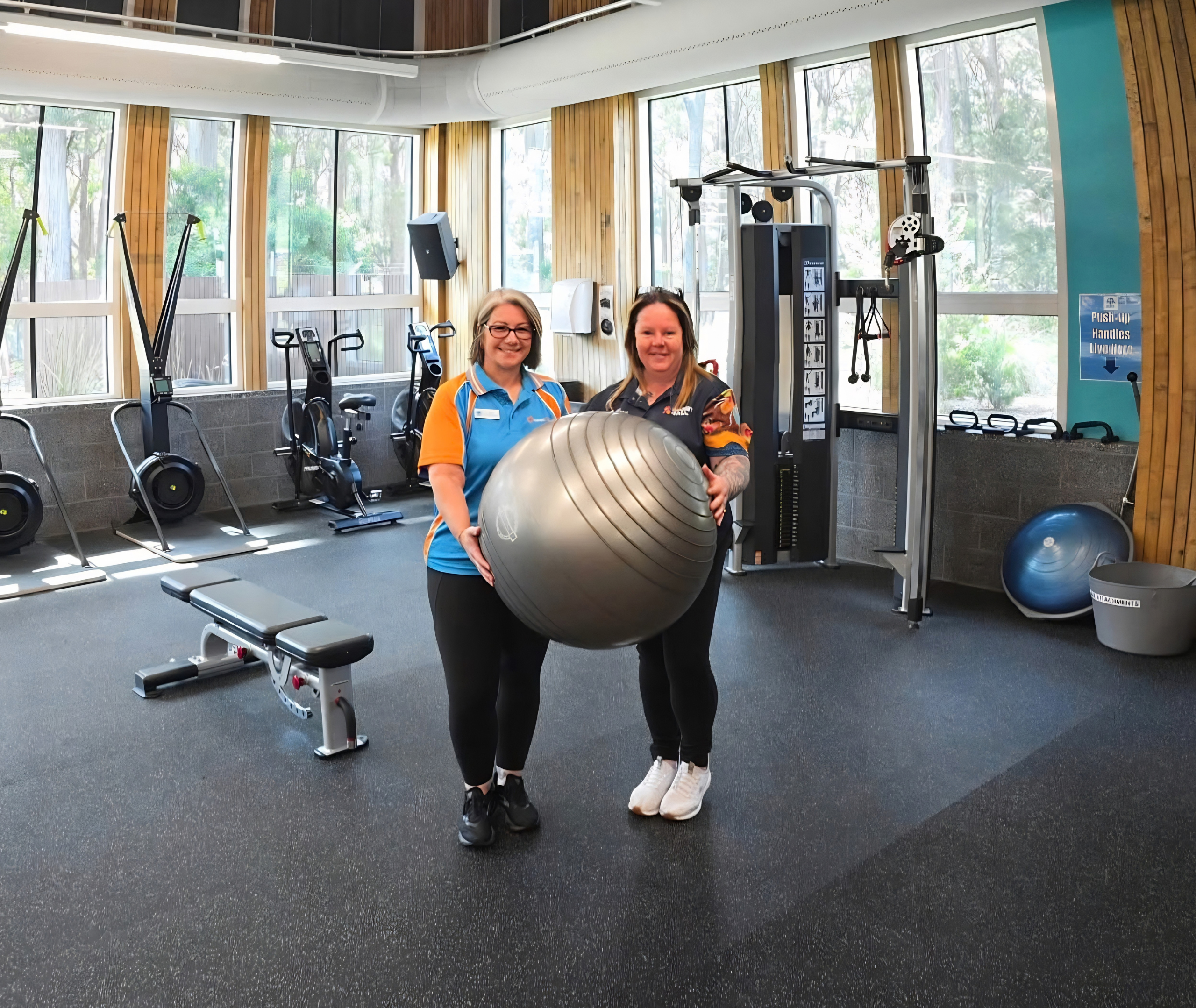 Jo alongside Splash staff stand in a gym holding a large exercise ball, surrounded by fitness equipment.
