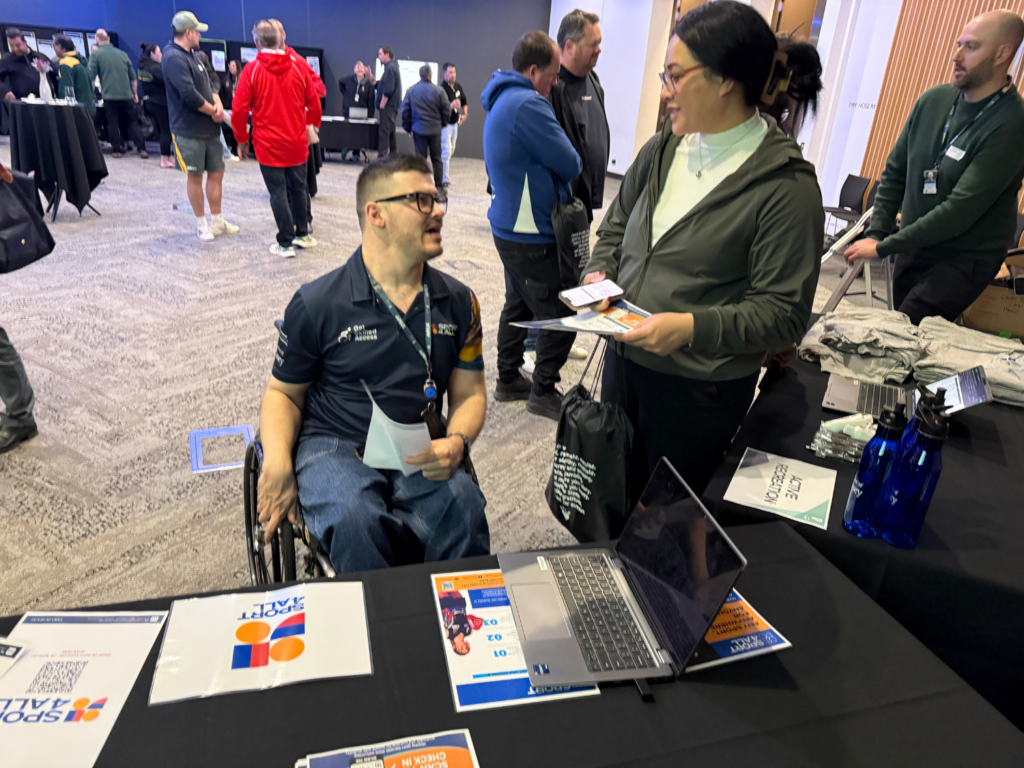 Oliver Hunter, Sport4All Inclusion Coach - City of Casey on a wheelchair speaks with an attendee at a Sport4All information stall during a community event.