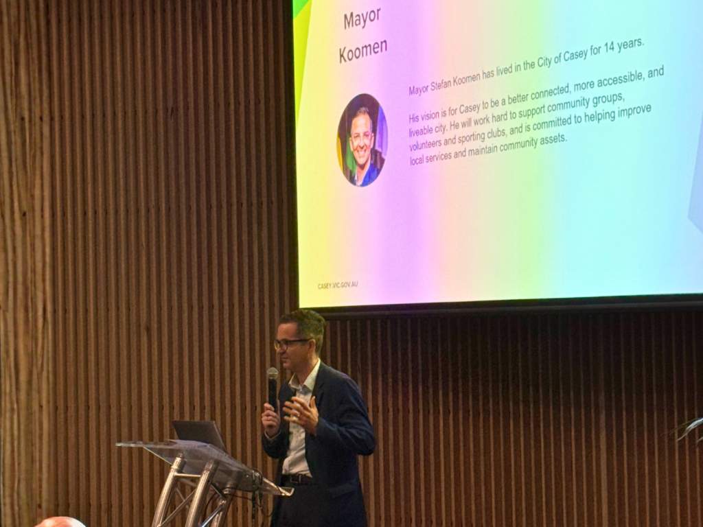 Mayor Stefan Koomen speaks at a City of Casey club development event, with a presentation slide about his vision for a more accessible and liveable city displayed behind him.