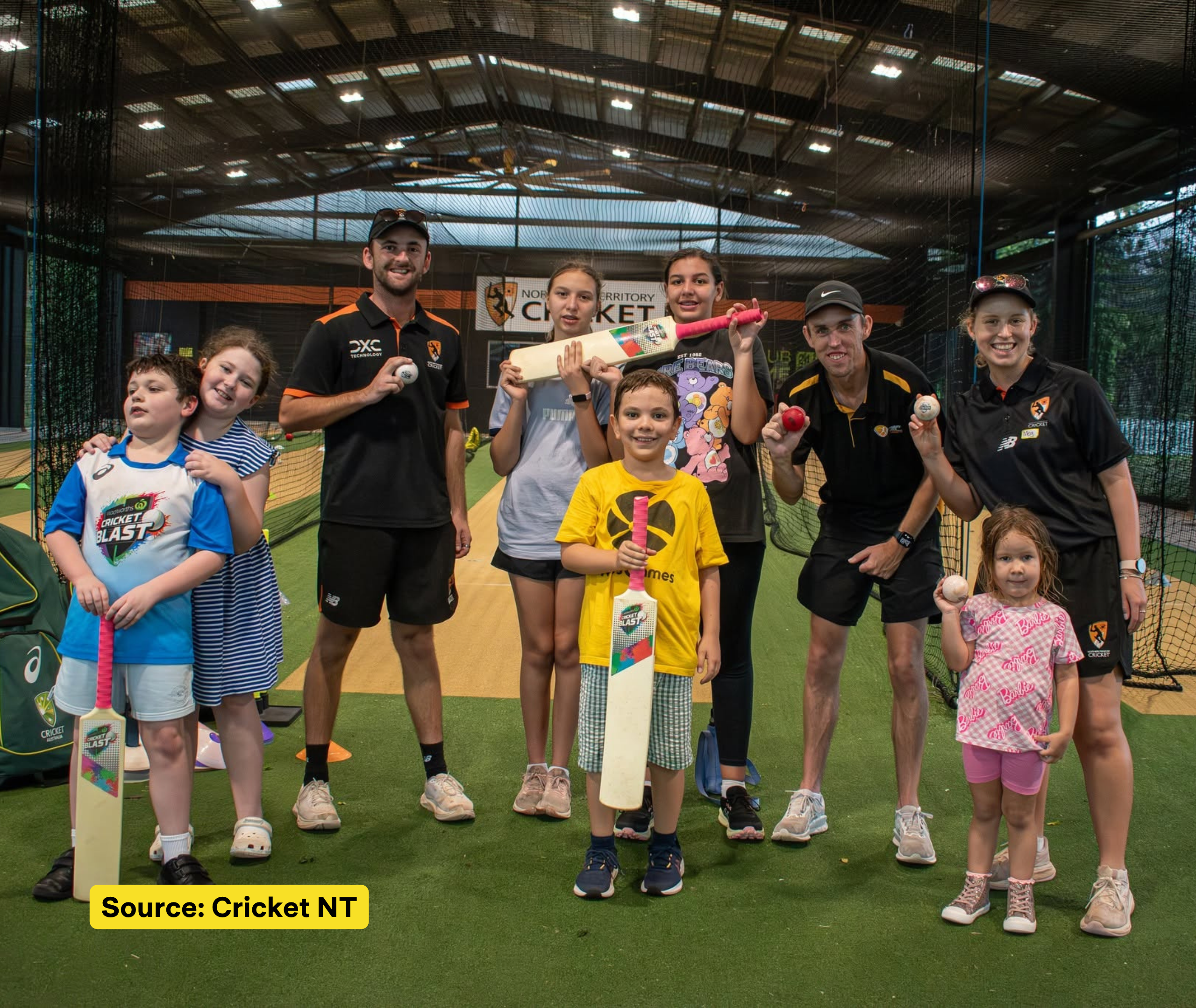 Children and Cricket NT staff pose with cricket bats and balls inside an indoor cricket net.