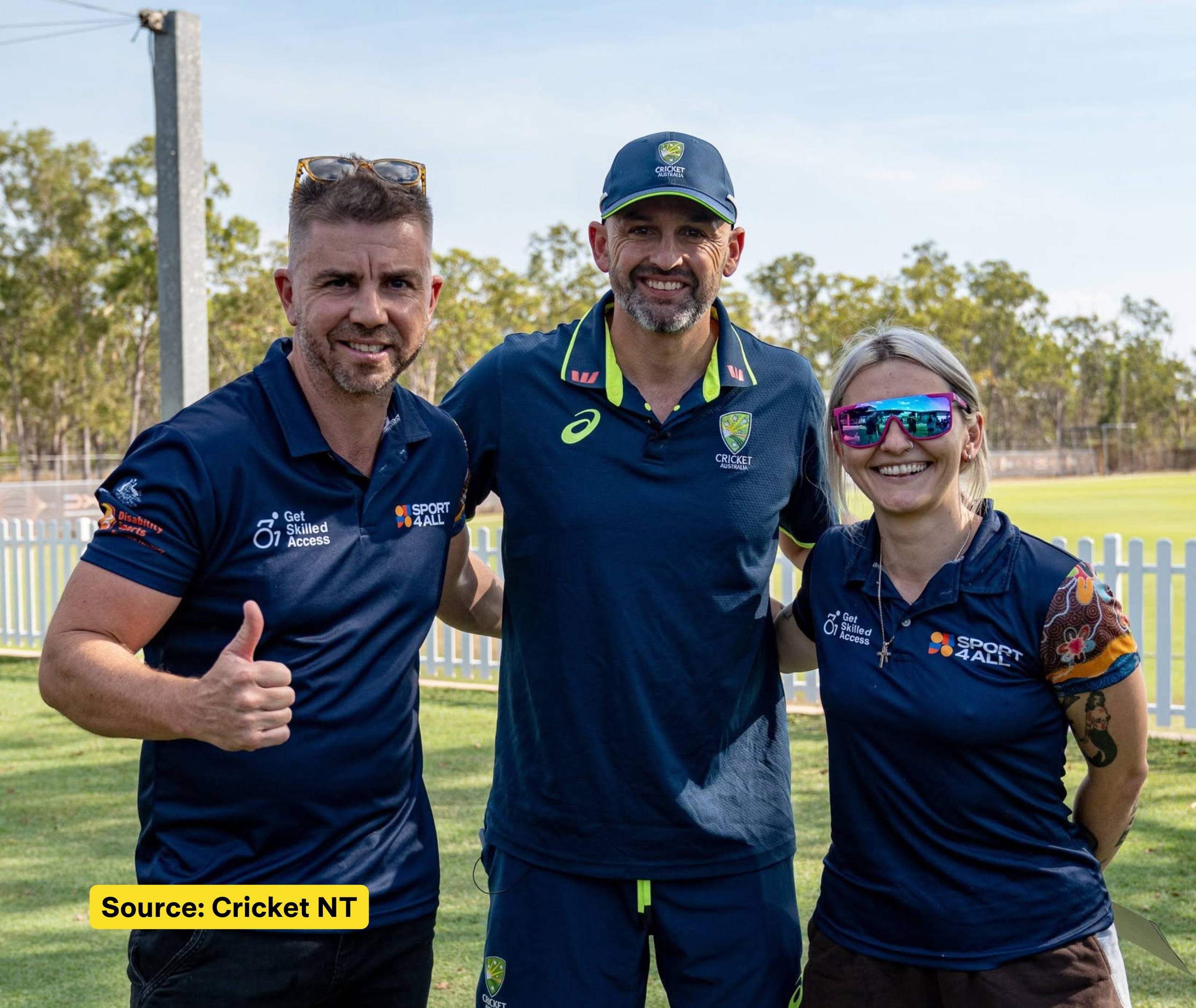 Two Sport4All team members stand beside Nathan Lyon in a Cricket Australia uniform at an outdoor cricket ground.