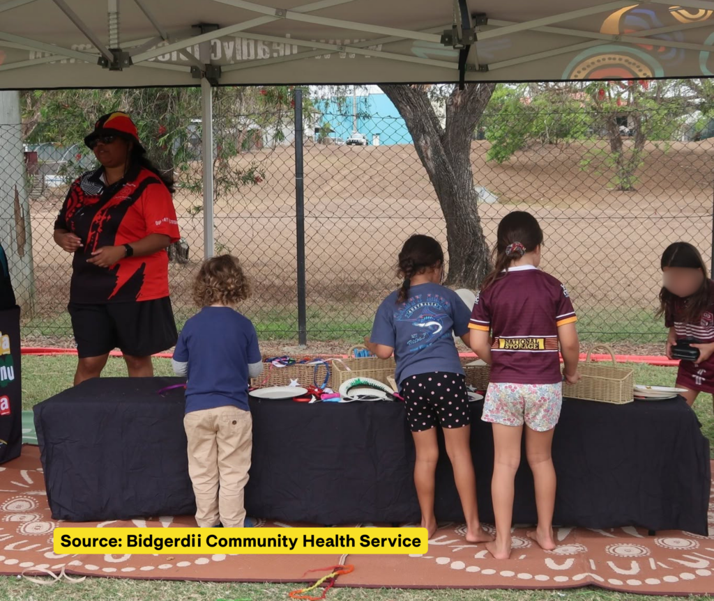 Children take part in craft activities at a table under an outdoor marquee, with an adult standing beside them.