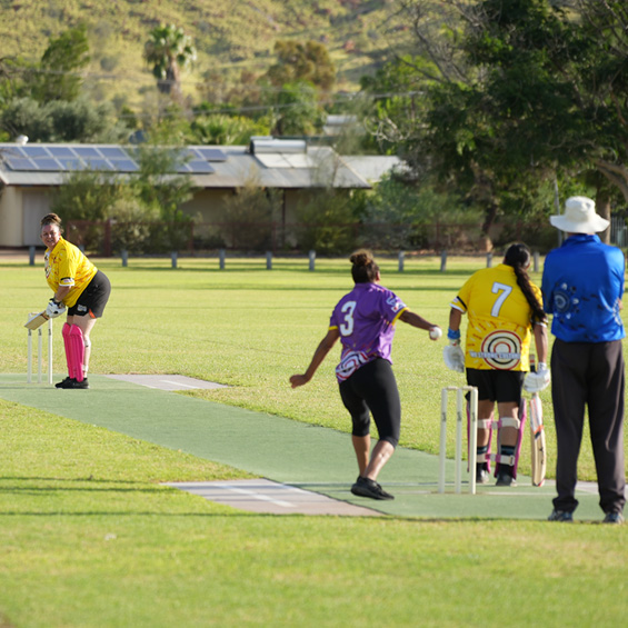 This photo shows a group of First Nations peoples playing cricket in the sun.